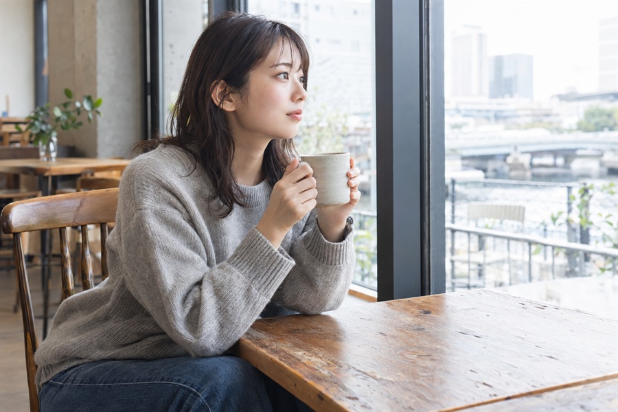 カフェの窓際でひと息つく20代の女性